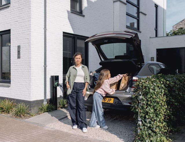 Vrouw en kind op oprit bij laadpaal thuis