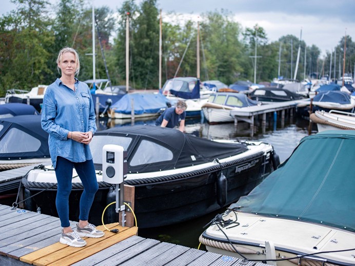 Vrouw in spijkerblouse bij een laadpaal in een jachthaven