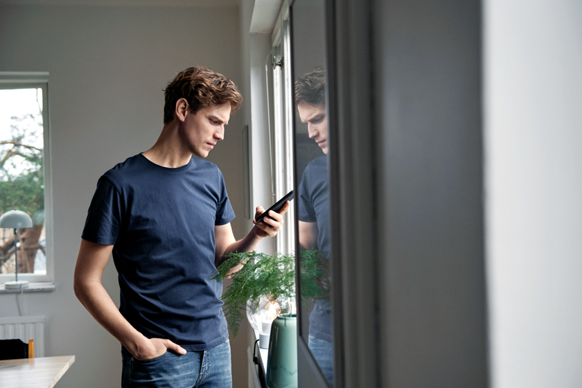 Jonge man in blauw t-shirt kijkt op telefoon - combineer stadsverwarming met stroom