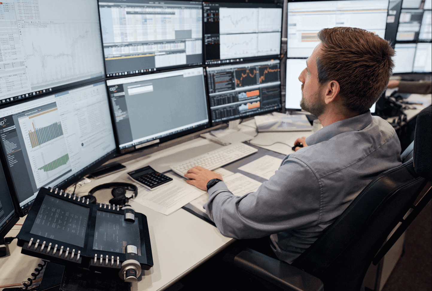 Man achter een bureau met daarop een serie van beeldschermen 