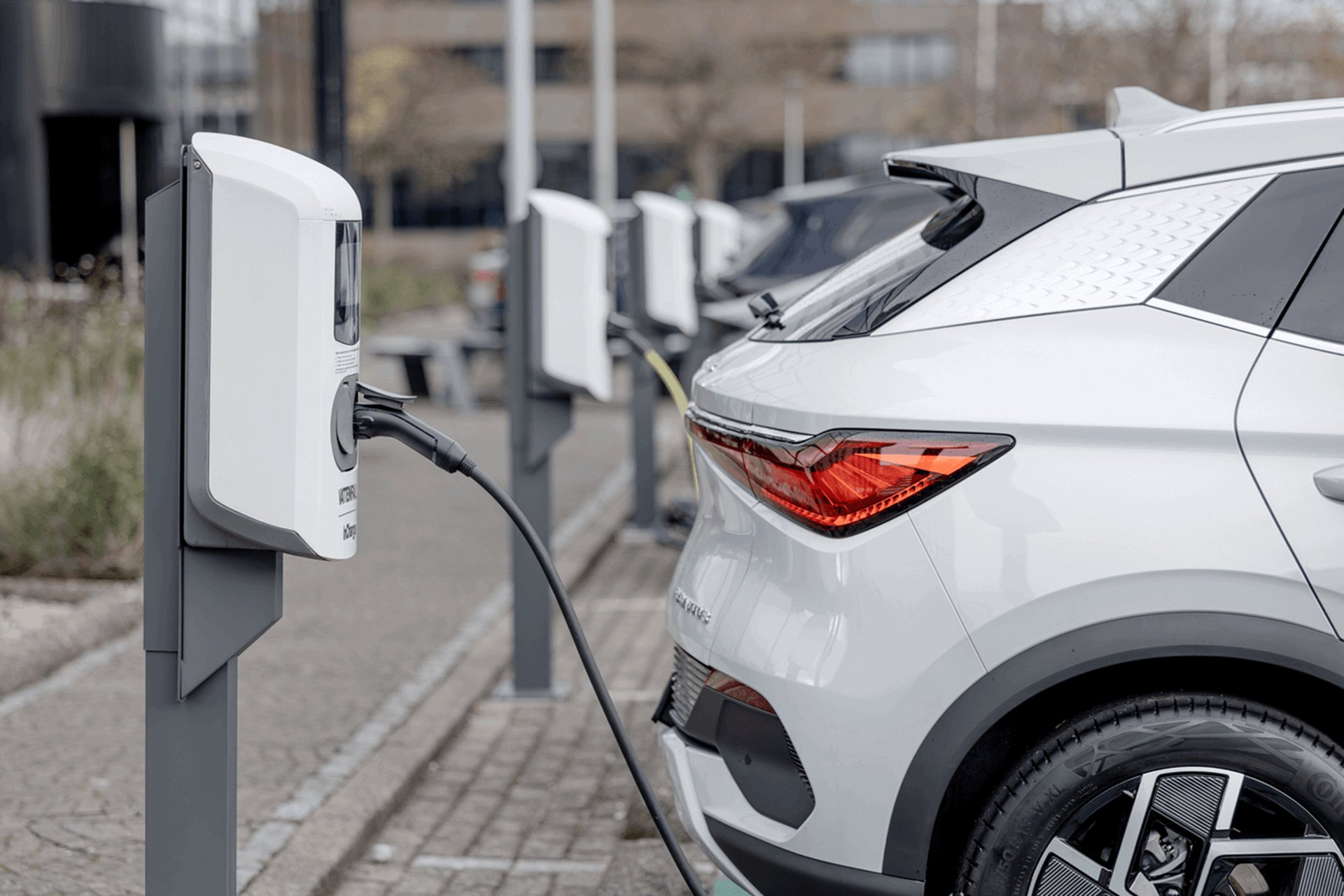 Vrouw staat met haar elektrische auto bij een laadpaal aan de kust