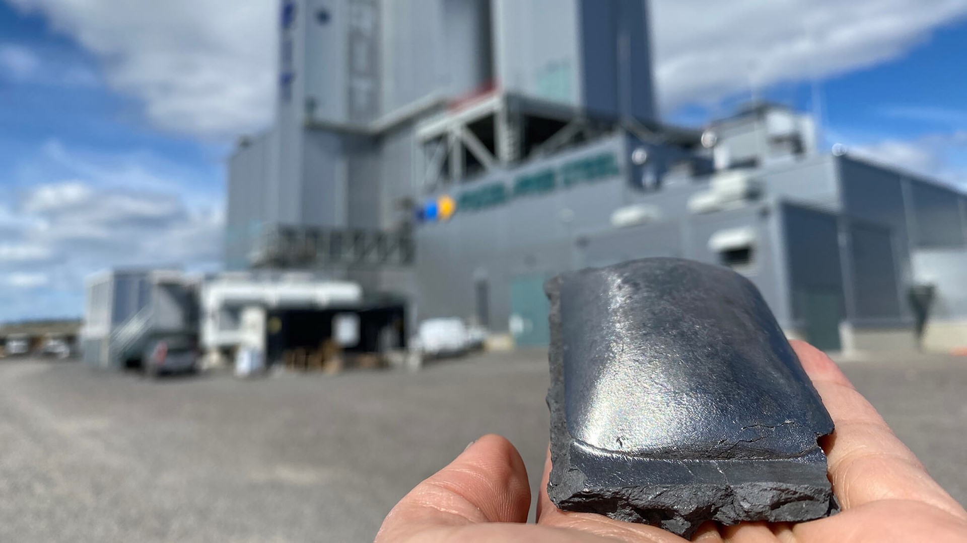 Man met sponsijzer in zijn hand met de HYBRIT fabriek op de achtergrond