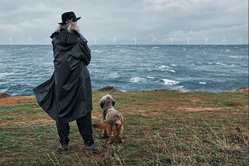 Man met hoed en hondje met op de achtergrond een windpark op zee