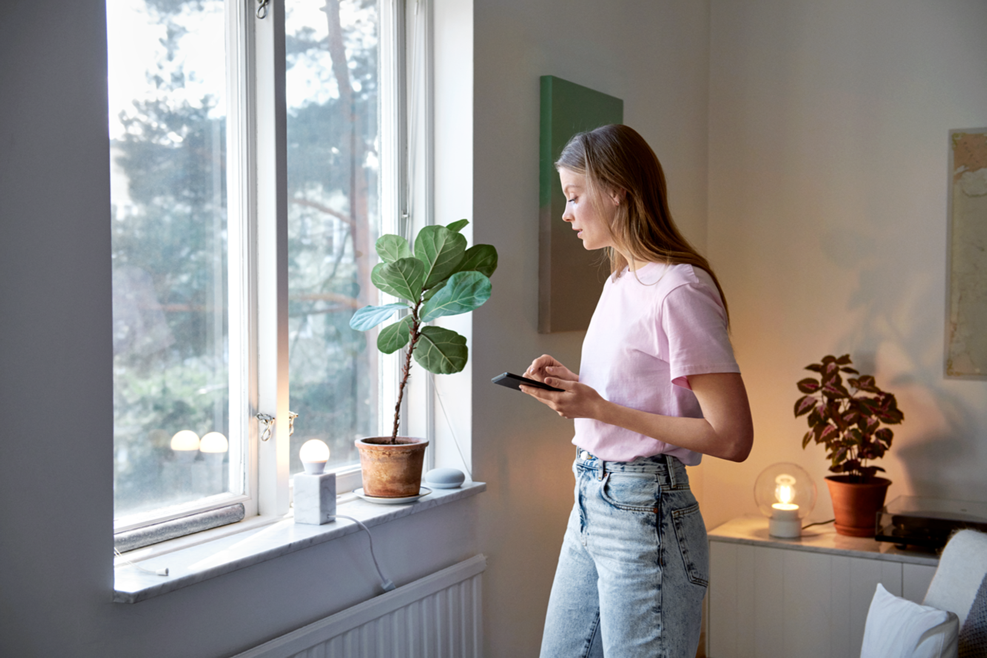 Mevrouw staat voor raam en kijkt op telefoon