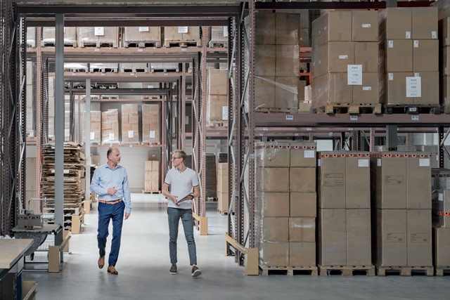 Twee mannen lopen in een magazijn vol met dozen