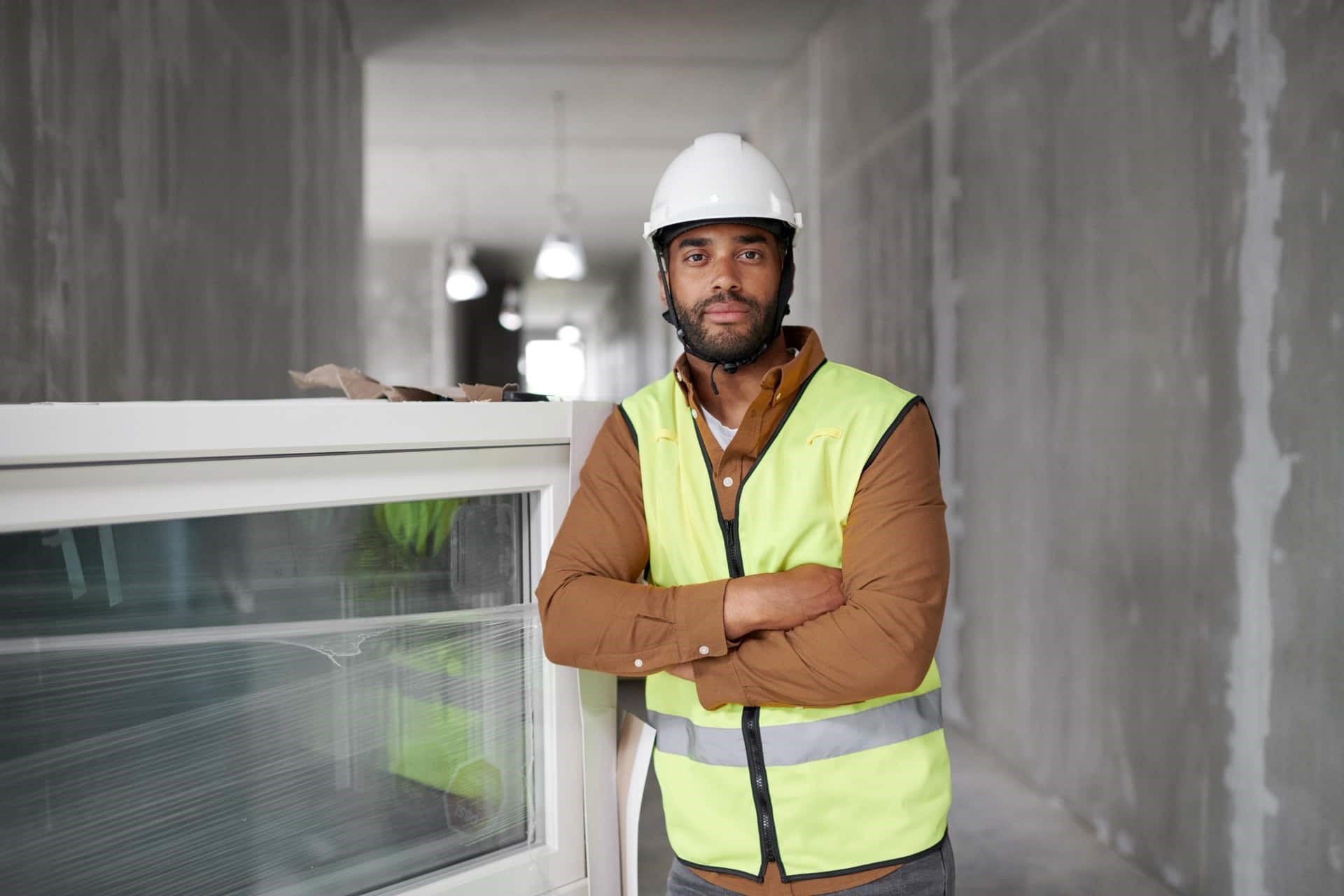 Man met geel hesje en witte helm in gebouw in aanbouw naast nieuw te plaatsen kozijn met HR++ glas