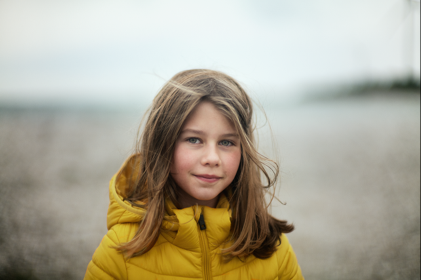 Meisje in gele jas met haren wapperend in de wind